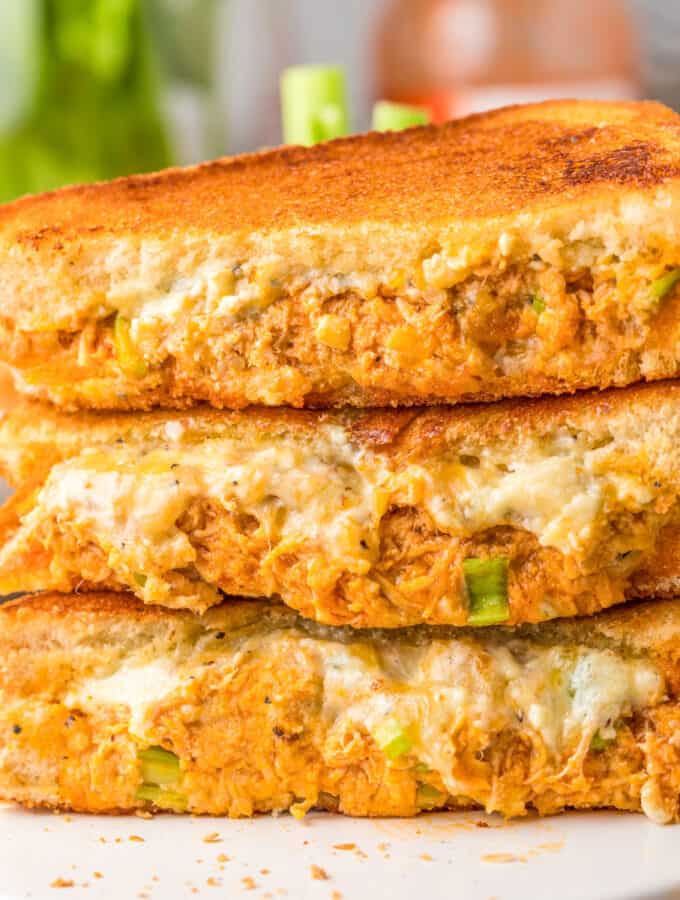 Close up square image of three sandwich halves stacked on top of one another on white platter.