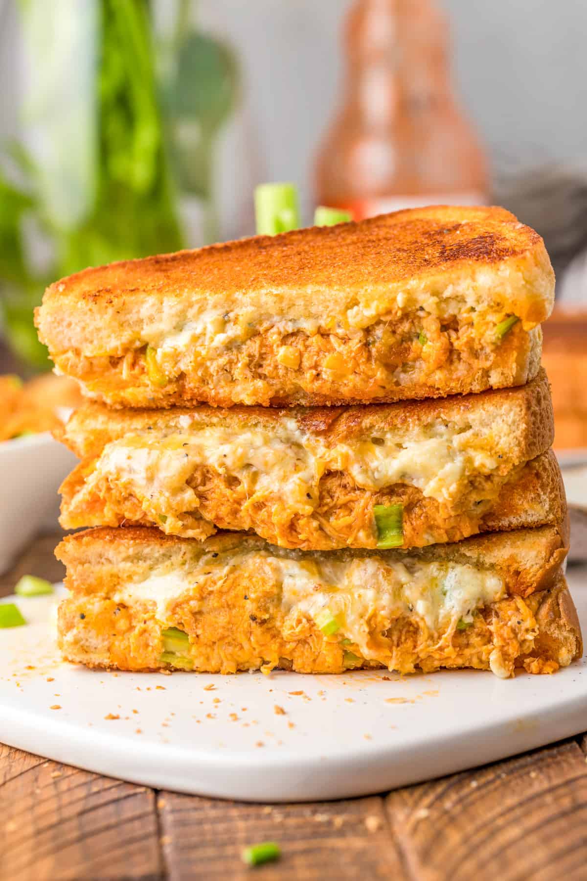 Three Buffalo Chicken Grilled Cheese halves stacked on top of one another showing inside on white platter.