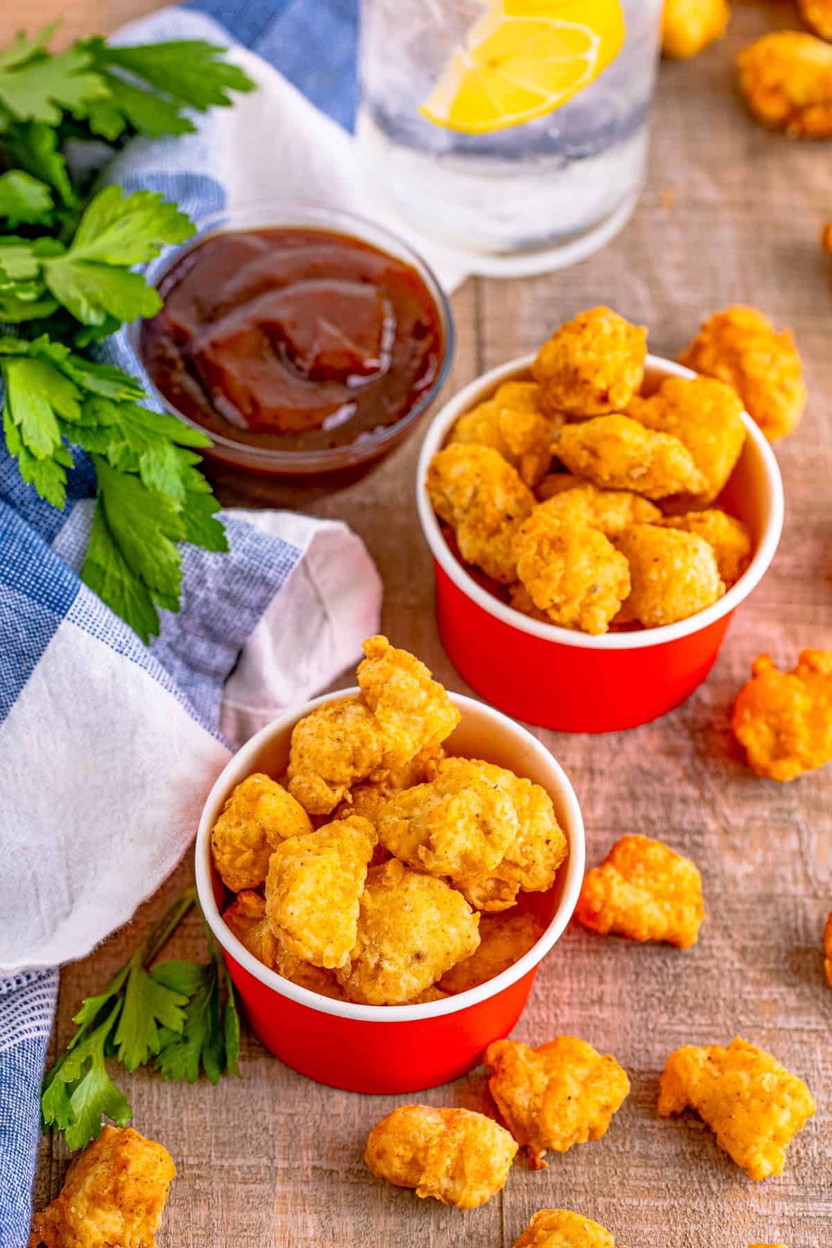 Slightly overhead of finished Popcorn Chicken in two red containers with BBQ sauce in background.