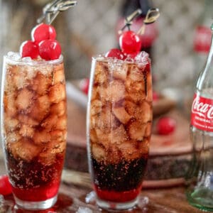 Close up square photo of two mocktails garnished with cherries.