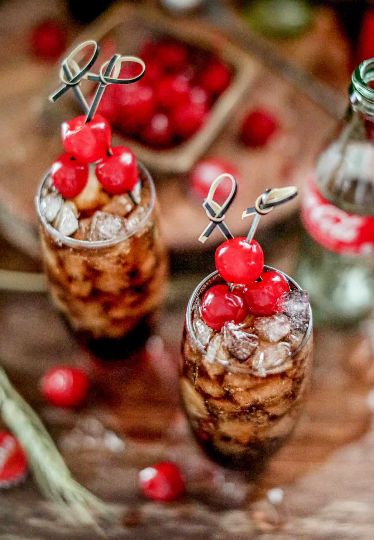 Overhead of finished drinks garnished with cherries and a cola bottle in background.