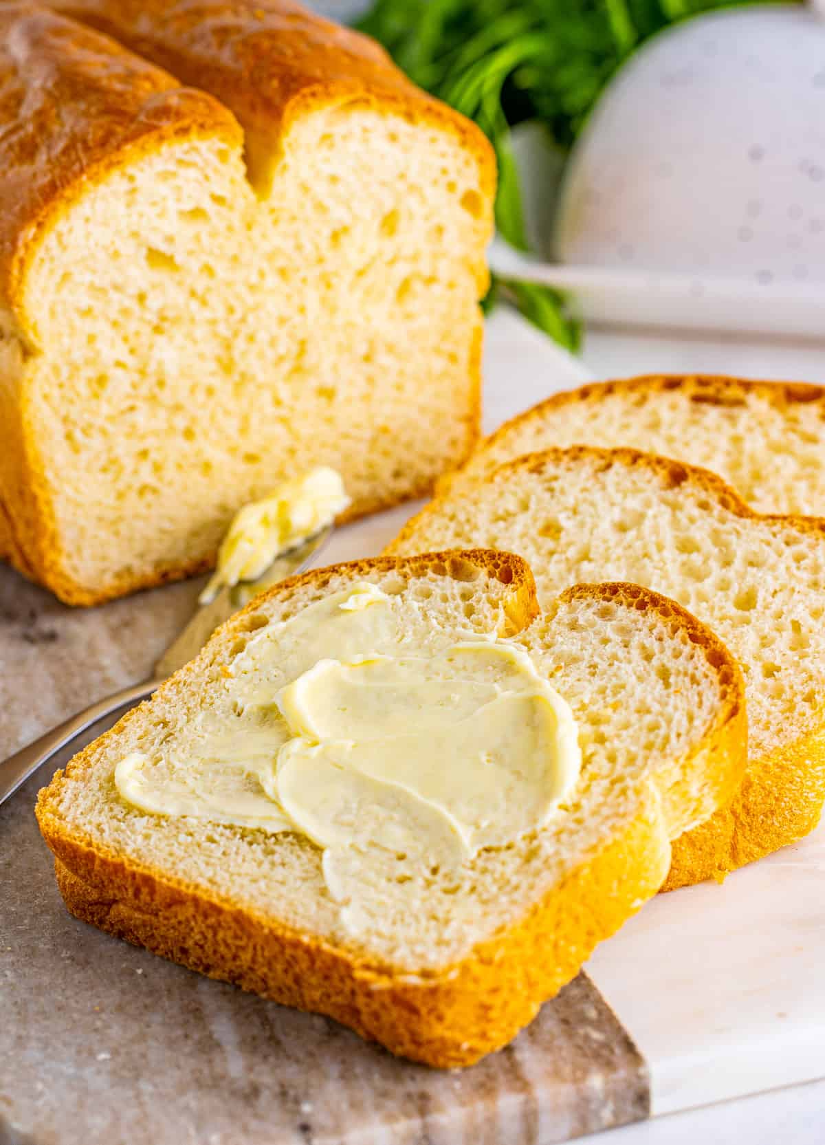 Finished White Bread Recipe with slices layered on one another with one slice covered in butter.