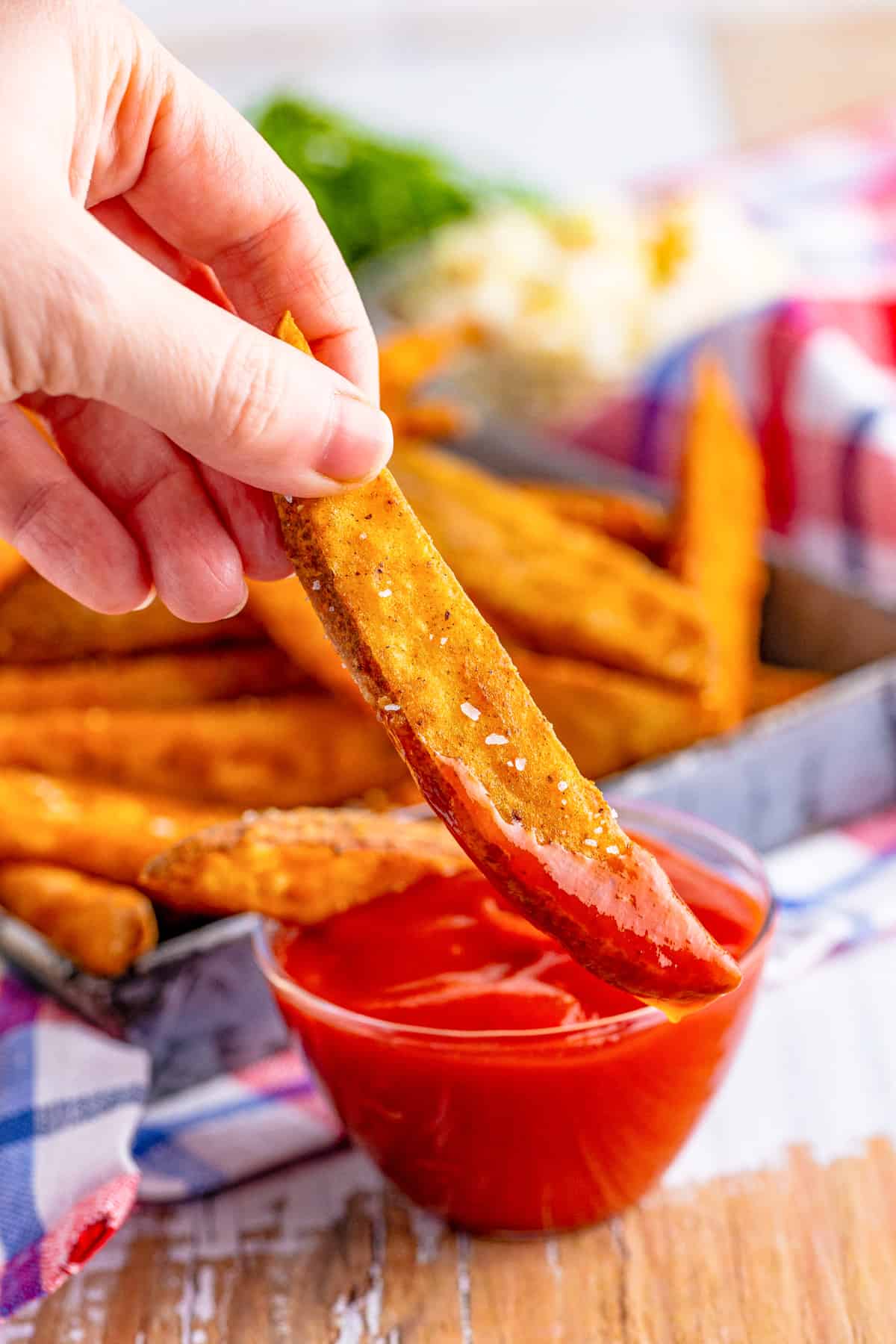 Hand holding up one Potato Wedge dipped in ketchup.