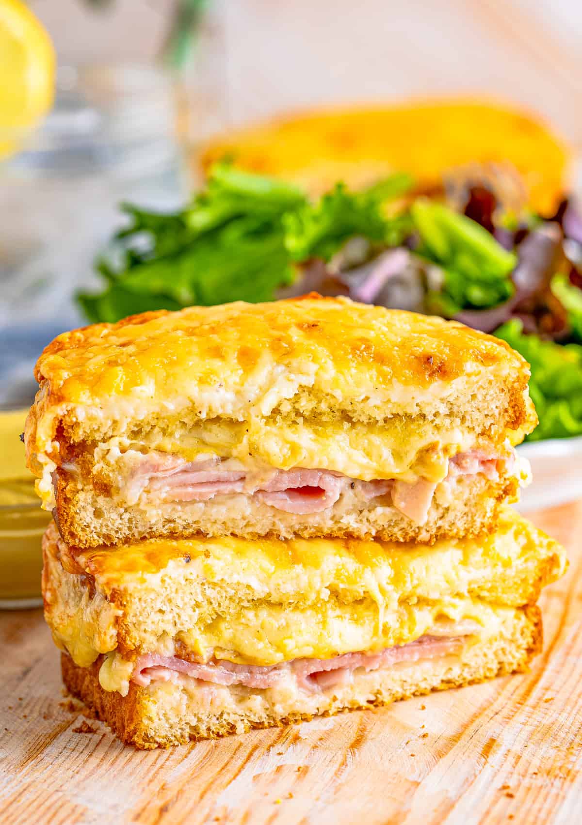 Croque Monsieur Recipe cut in half with the two halves stacked on top of one another showing inside sandwich with salad in background.