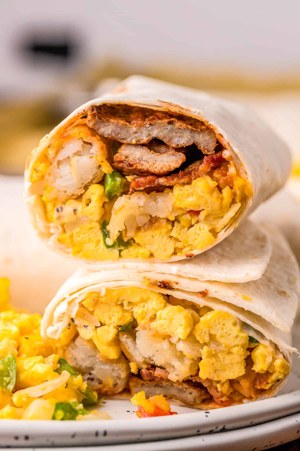 Finished Breakfast Burrito Recipe cut in half and stacked on top of one another on white plate showing inside of burritos.