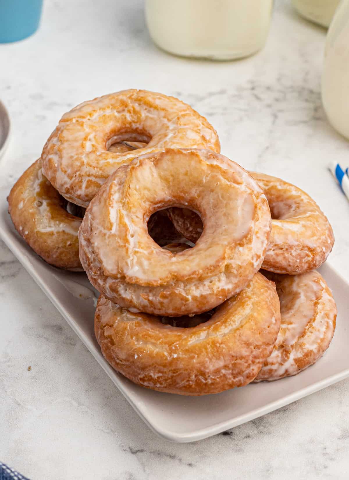 Donuts stacked on top of one another on a white longer tray with milk in background.