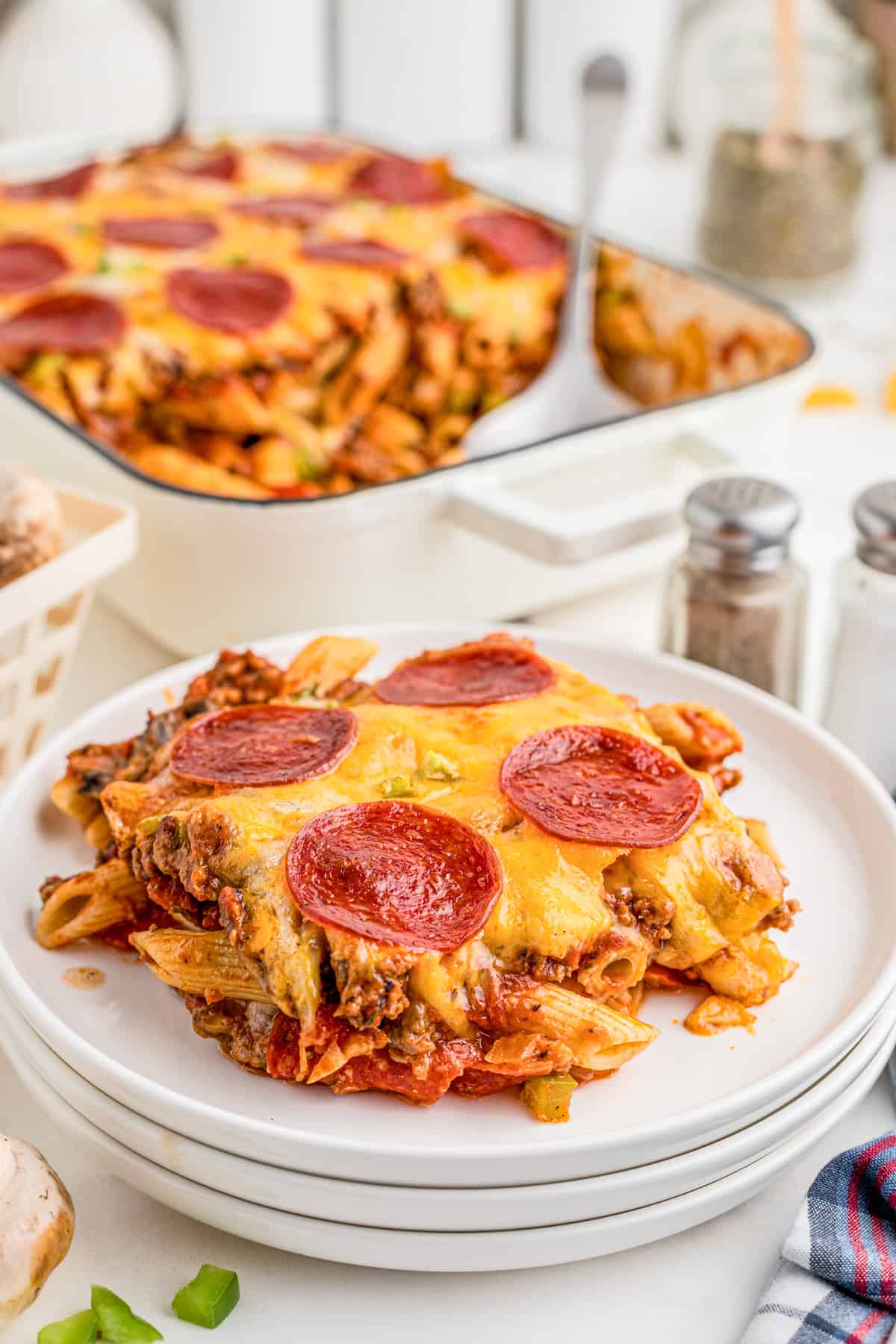 Pizza Casserole on white plate with the baking pan with remaining casserole in background.