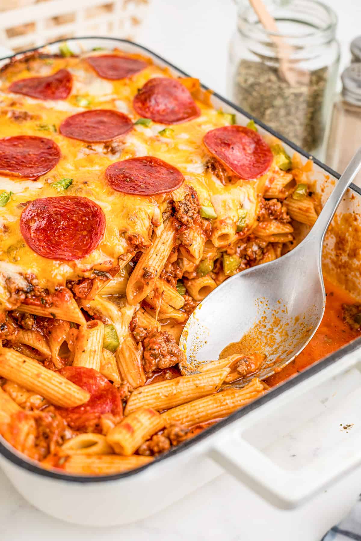 Pizza Casserole in baking pan with some scooped out with serving spoon in pan.