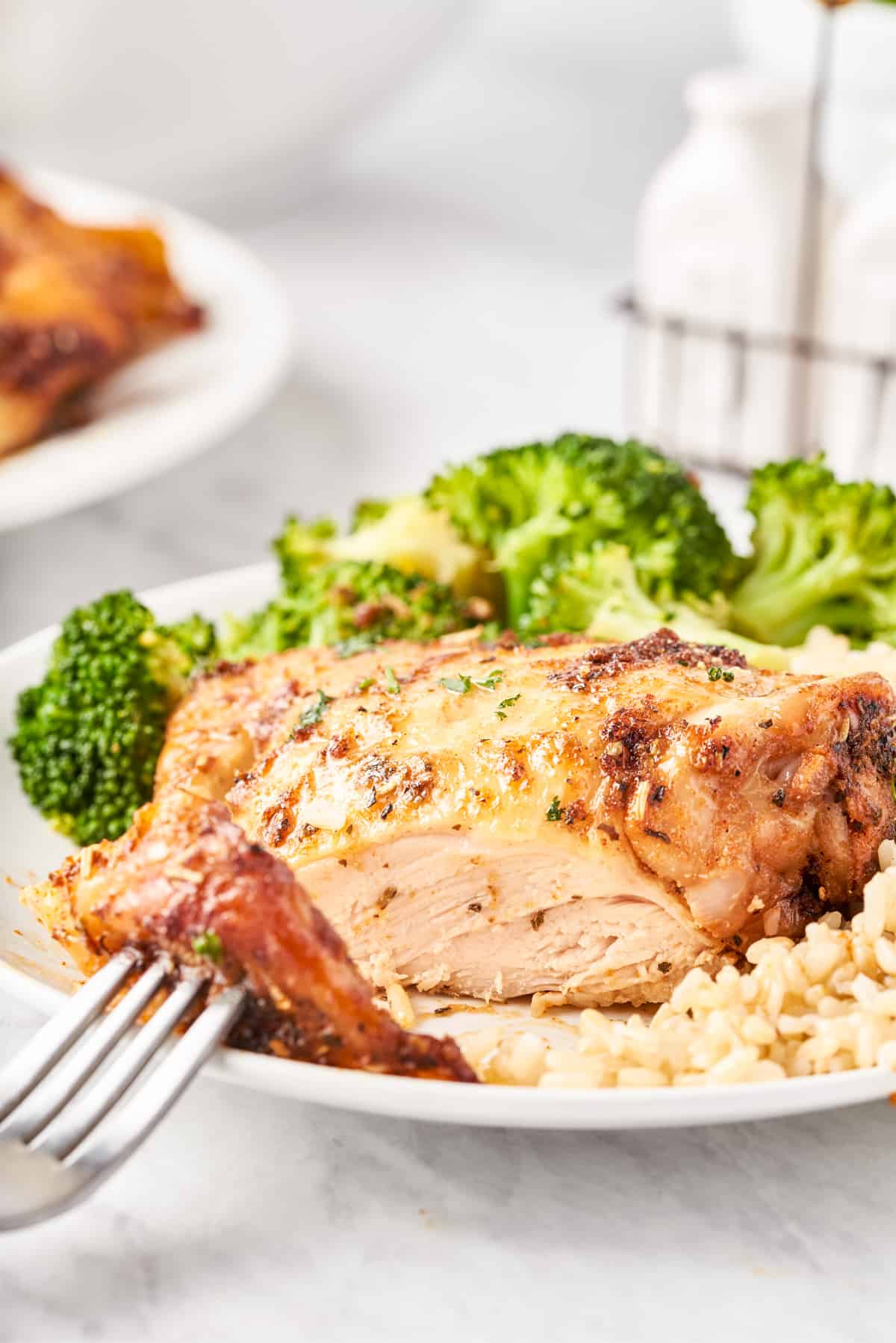 One chicken thigh on white plate with rice and broccoli cut open showing cooked inside.