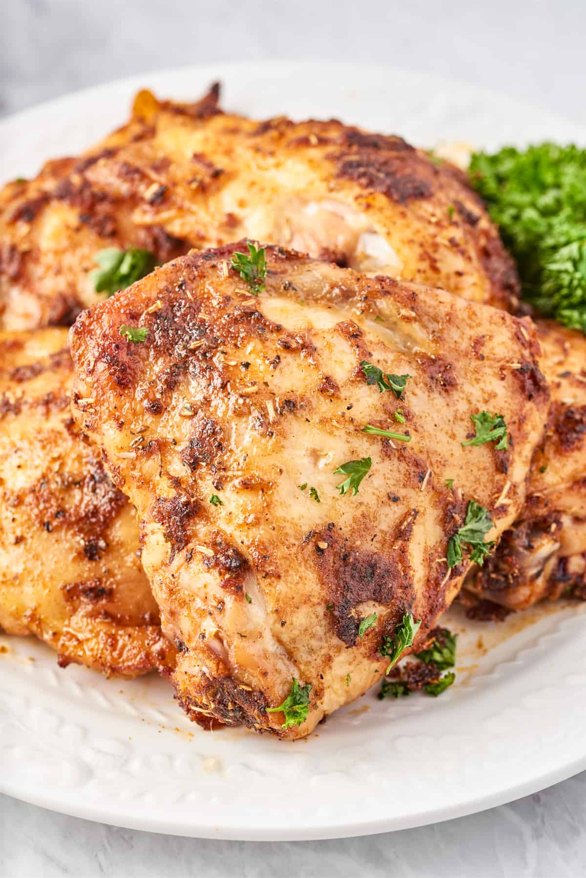 Stacked Roasted Chicken Thighs on white plate topped with parsley.