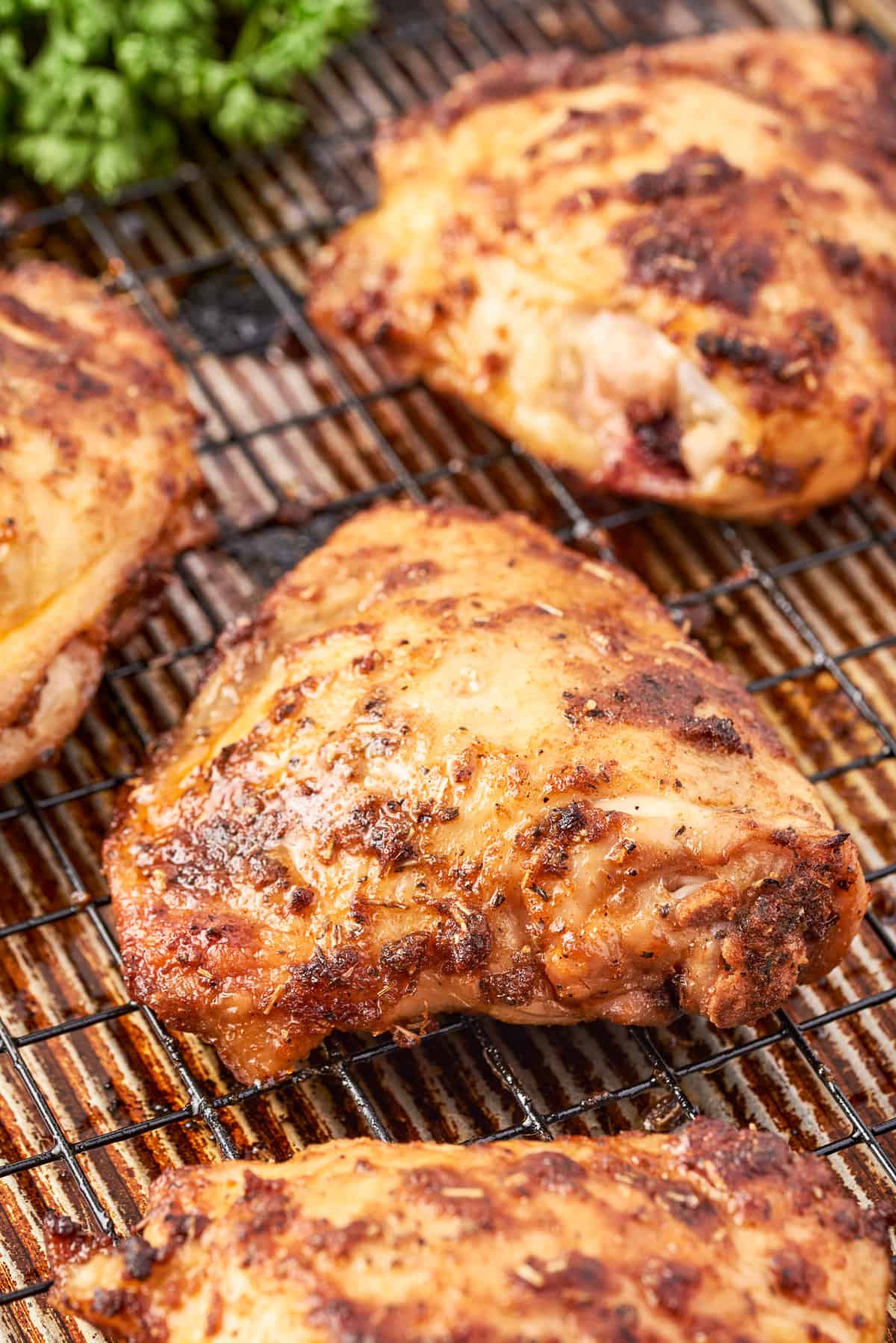 Finished Roasted Chicken Thighs on wire rack over a baking sheet with parsley in background.