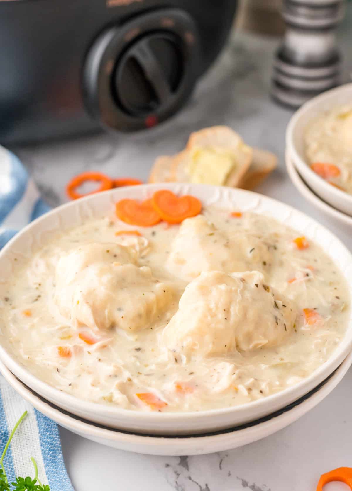 Finished Slow Cooker Chicken and Dumplings in white bowl with slow cooker in background.