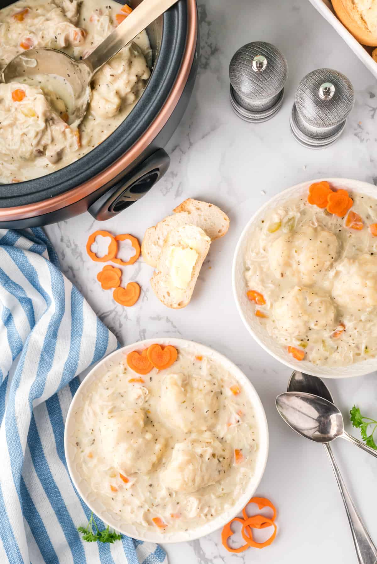 Overhead of two bowls of the chicken and dumplings and remainder in slow cooker.