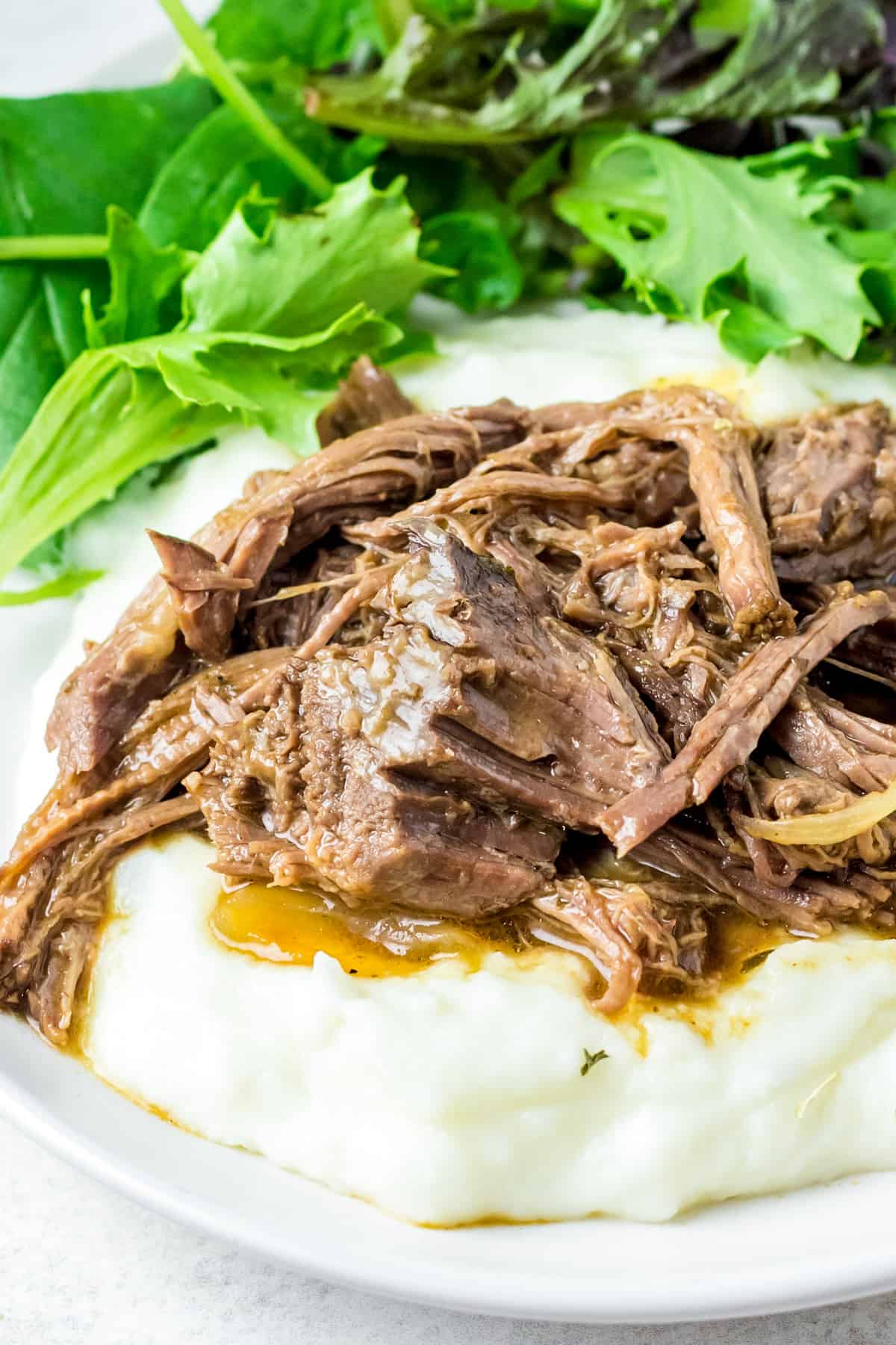 Slow Cooker Shredded Beef served over mashed potatoes on white plate with salad.