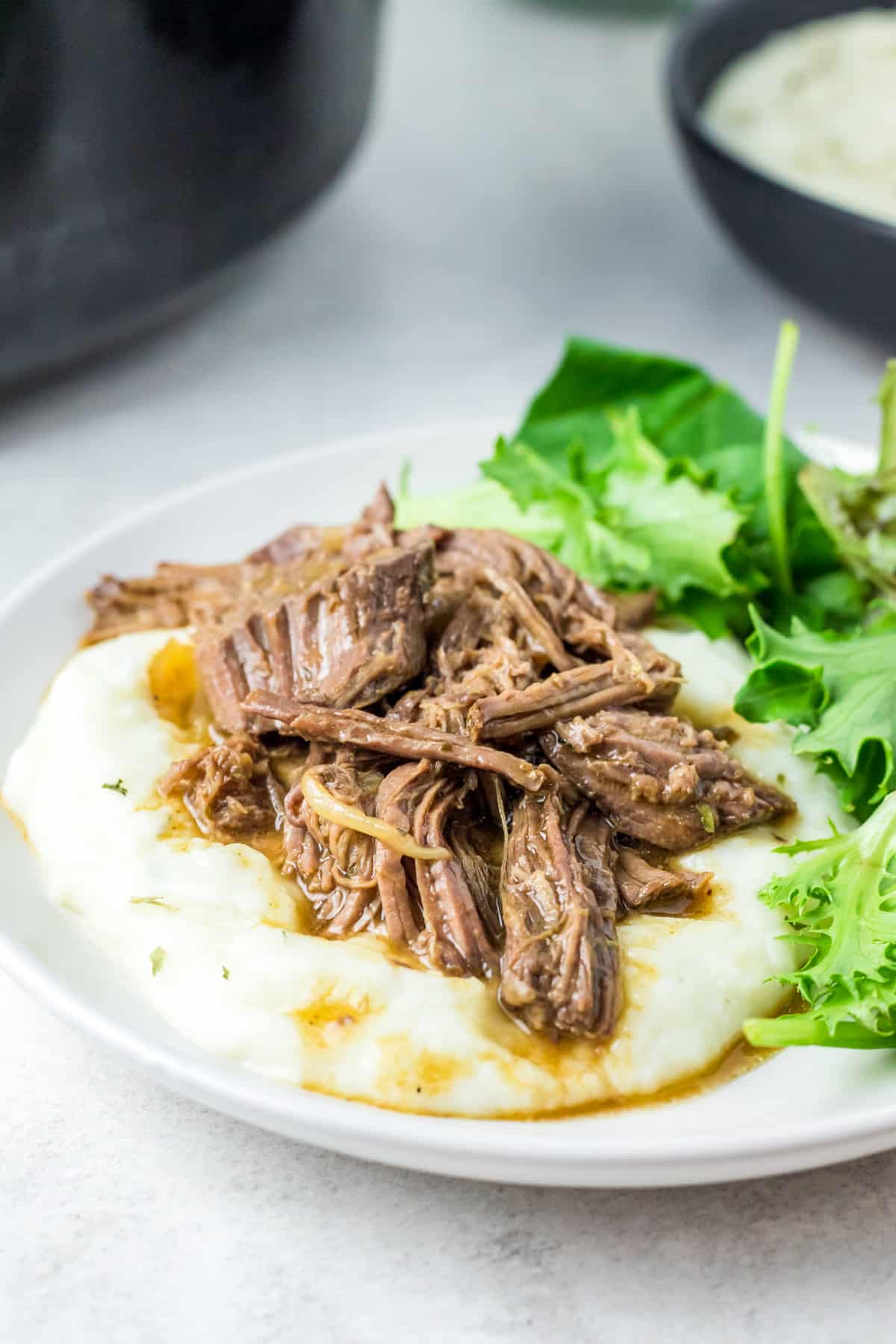 Slow Cooker Shredded Beef over mashed potatoes with a side salad on white plate.