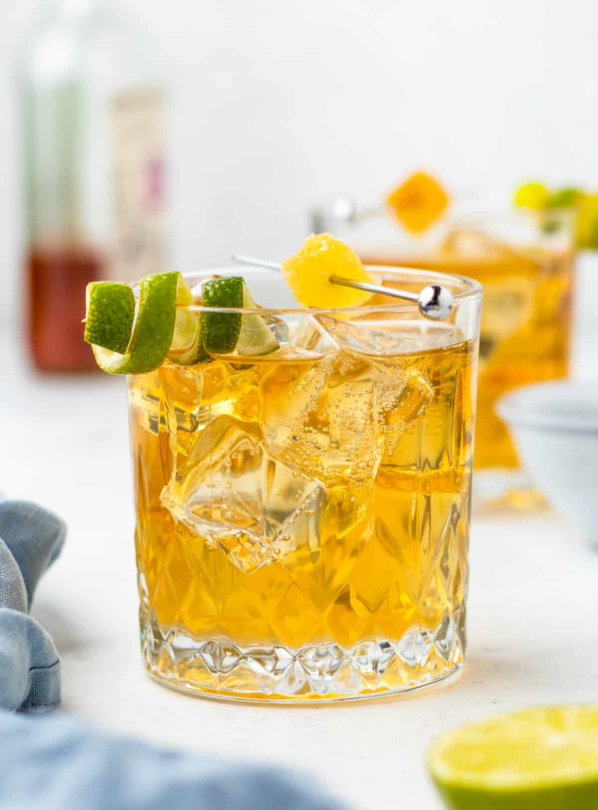 Finished Whiskey Ginger in glass with ice topped with a skewered candied ginger and a lime twist.