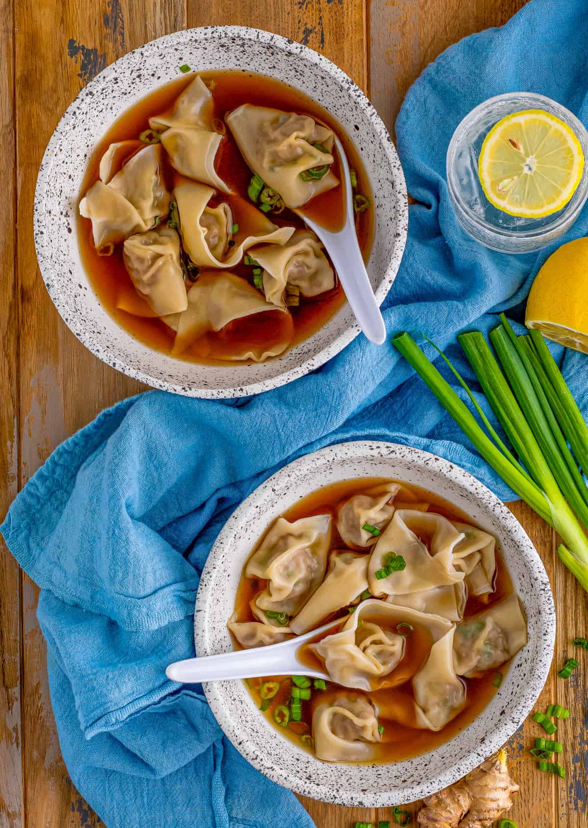 Overhead photo of two bowls of Wonton soup with green onions and ginger around bowls.