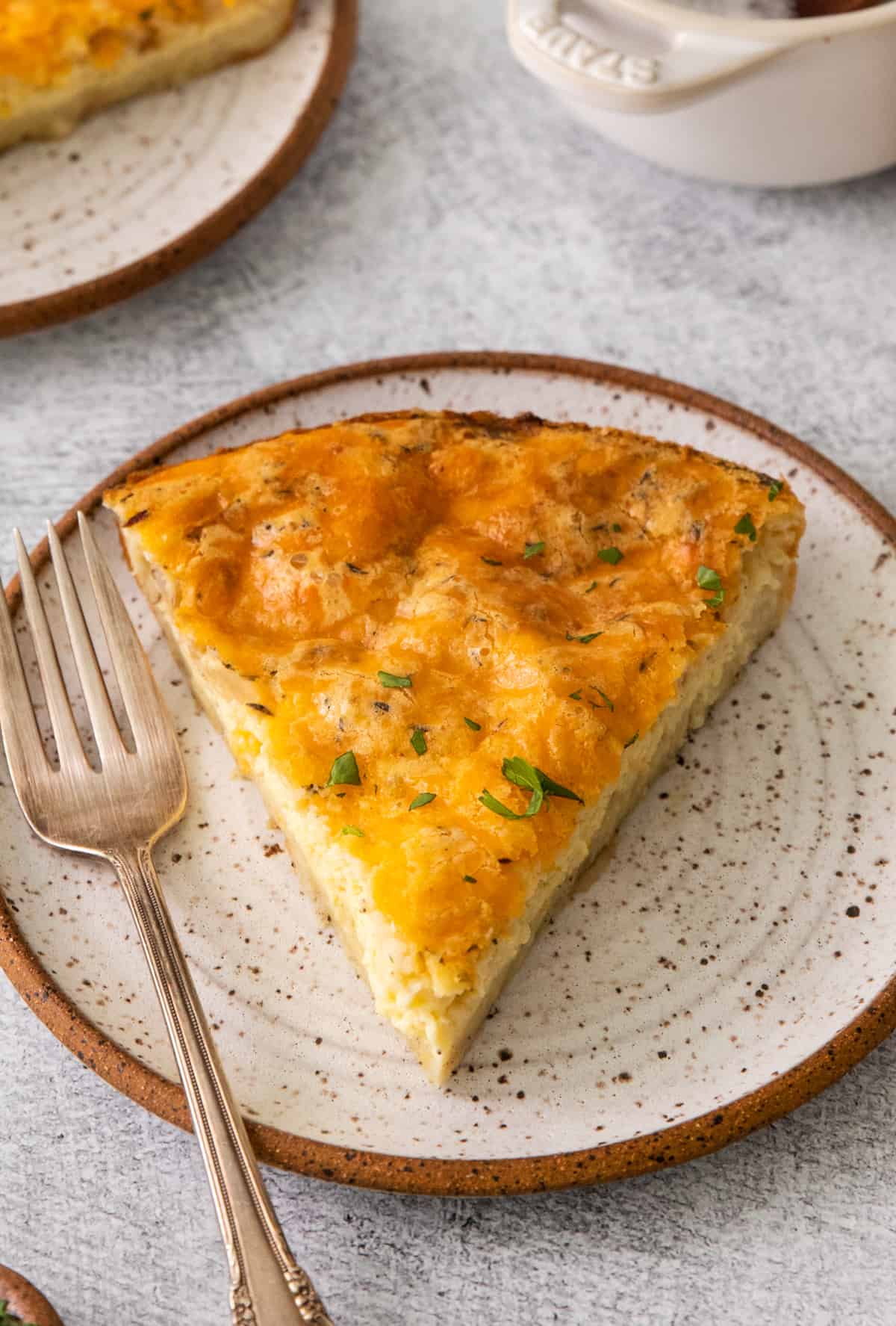A slice of the Bisquick Quiche on white speckled plate with fork.