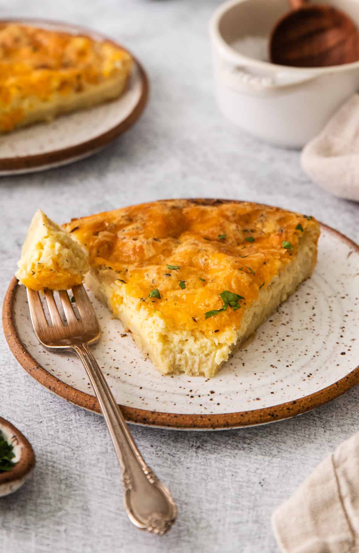 Slice of the Bisquick Quiche on a white speckled plate with bite on fork next to slice.