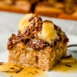 Close up photo of a slice of cake on a white plate topped with caramelized bananas and chocolate shavings.