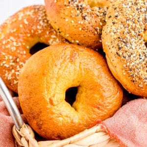 Close up square image of bagels in basket with pink linen and various toppings.