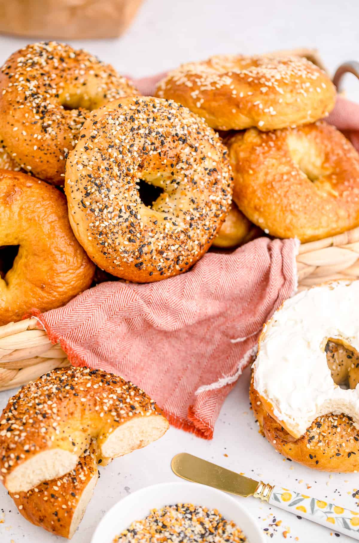 Homemade Bagels in basket with pink linen, one with cream cheese and one cut in half.