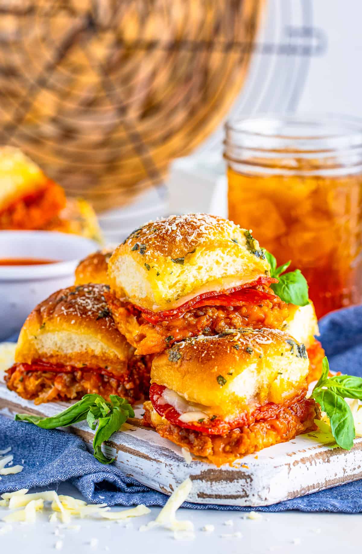 Pizza Sliders stacked on a white board with basil and tea in background.
