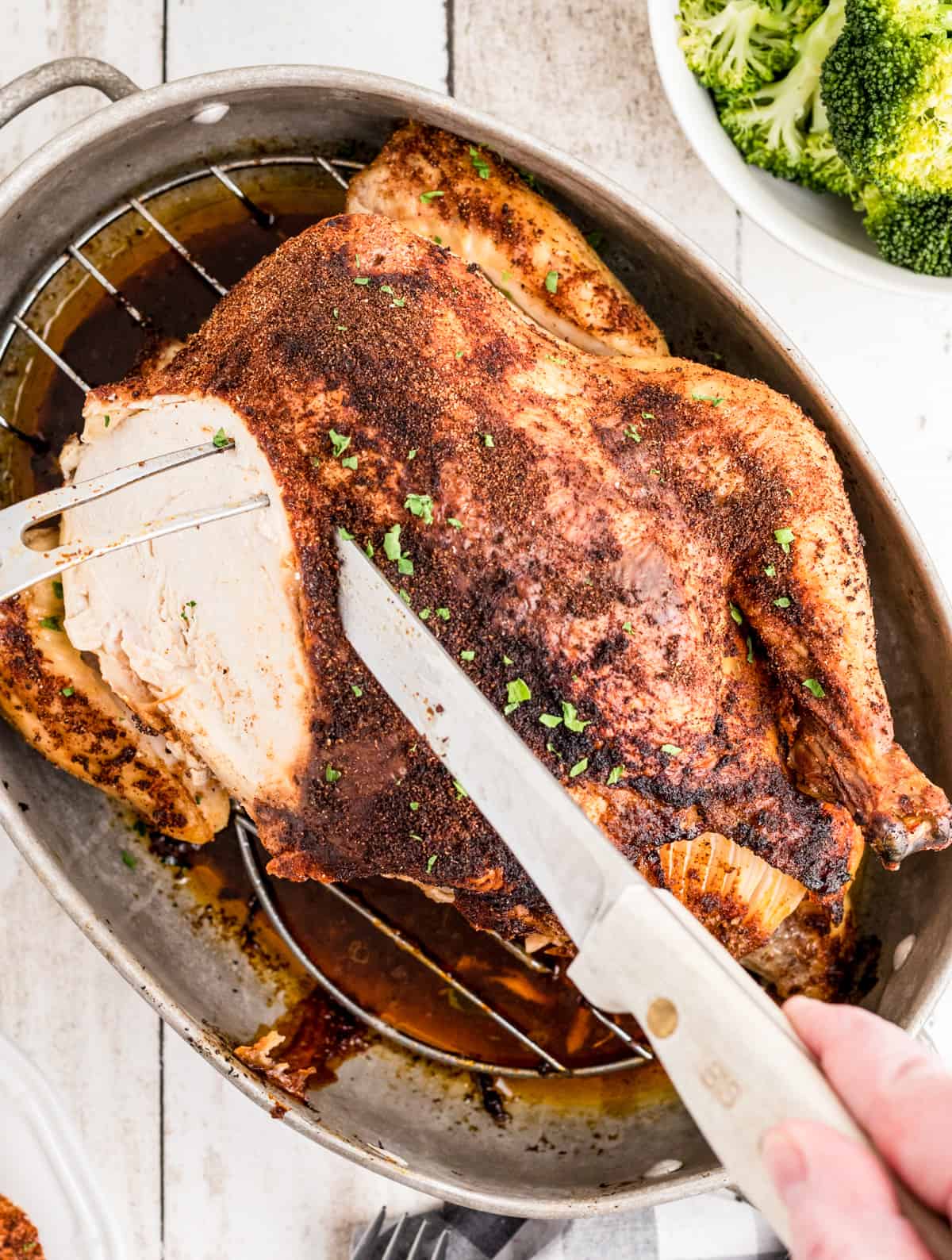 Overhead of hands carving chicken in roasting pan.