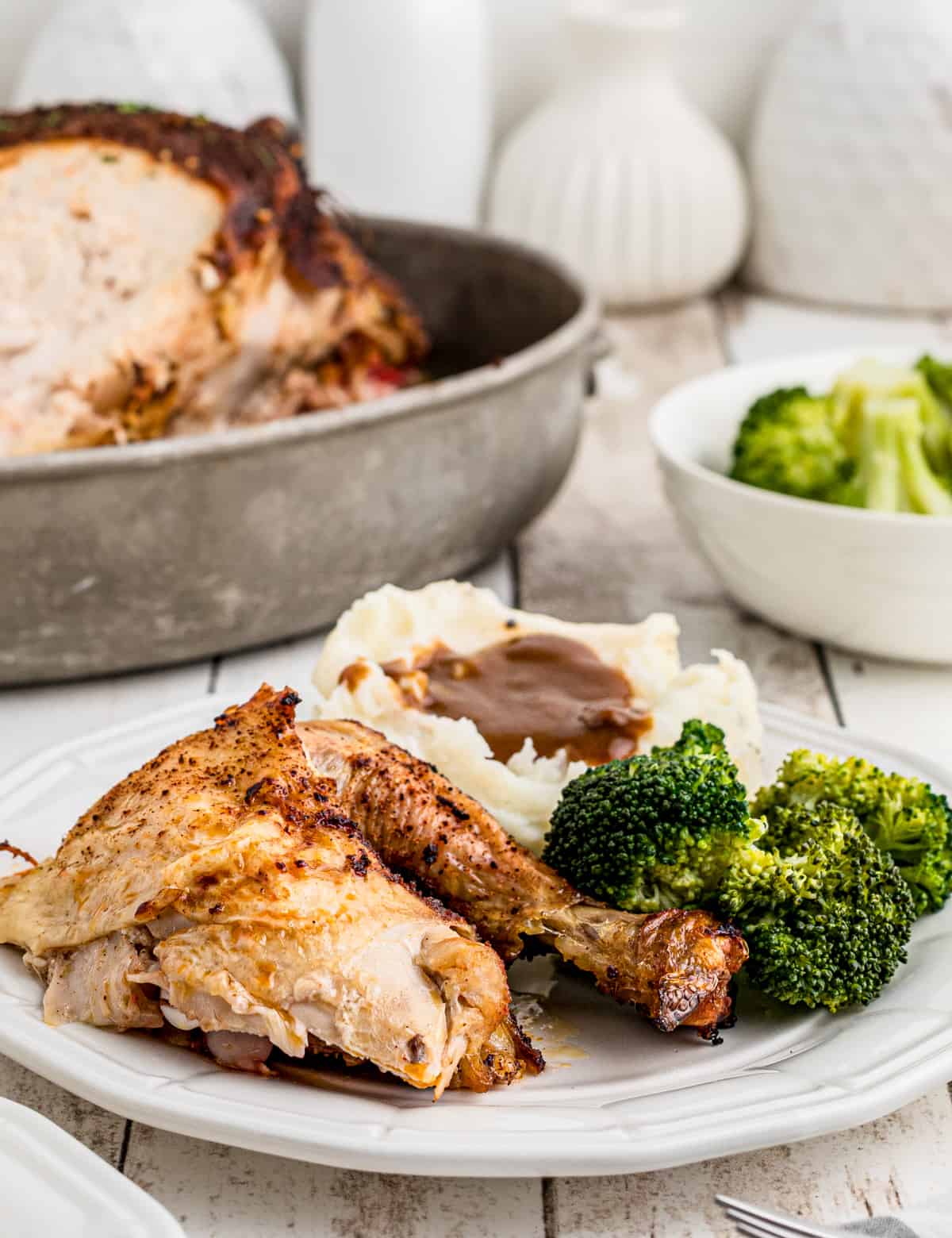 Plate of a piece of chicken, potatoes and broccoli with whole chicken in background.