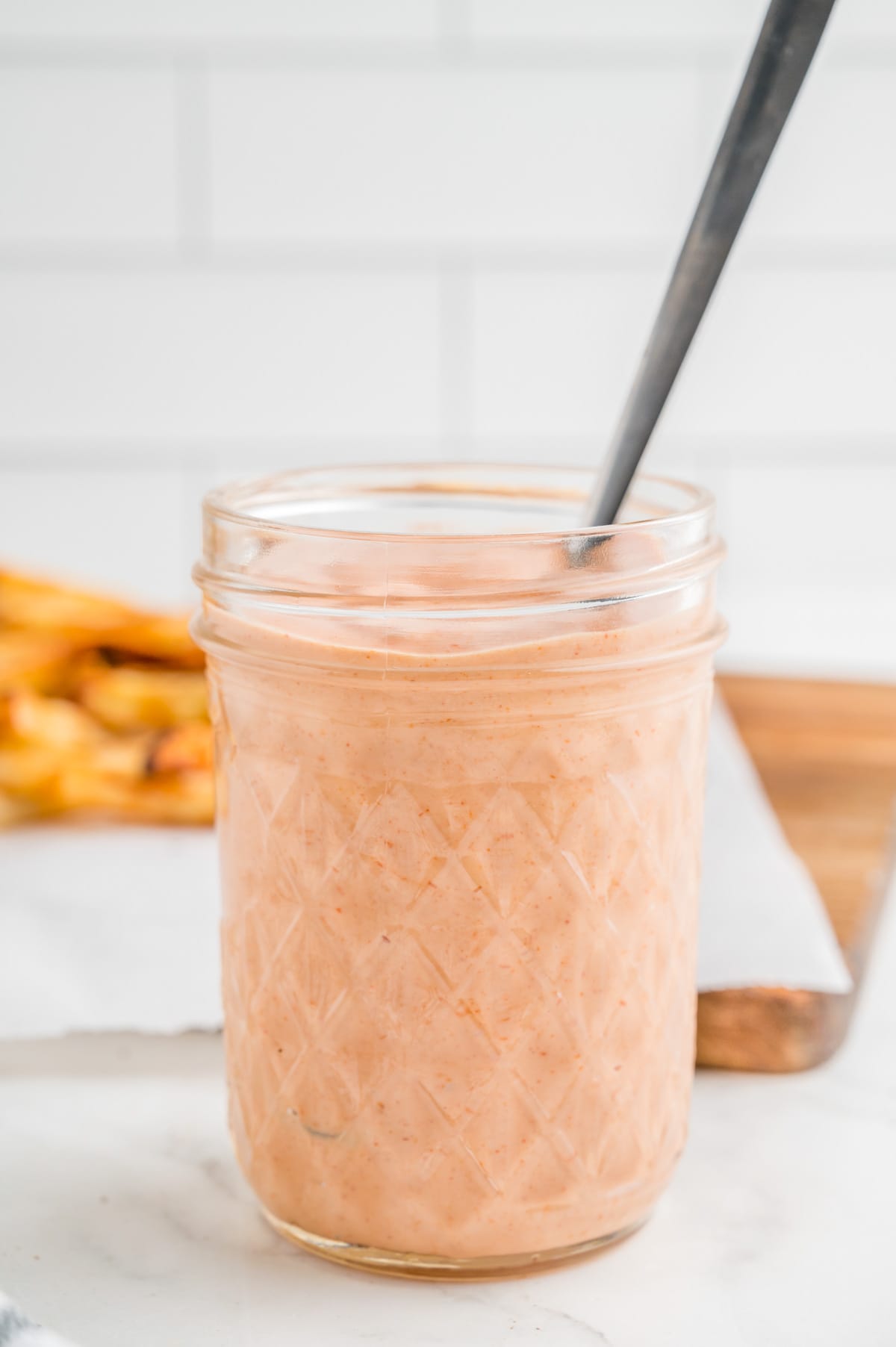Fry Sauce in glass jar with spoon in jar with fries in background.