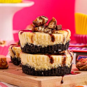 Closeup square image of two stacked cheesecakes with garnishes on wooden board.