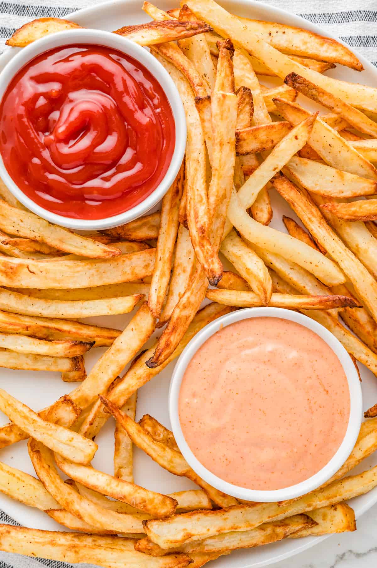 Overhead of fries on white plate with bowls of ketchup and fry sauce.