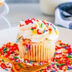 Close up square image of cupcake on white plate with sprinkles and a gold fork.