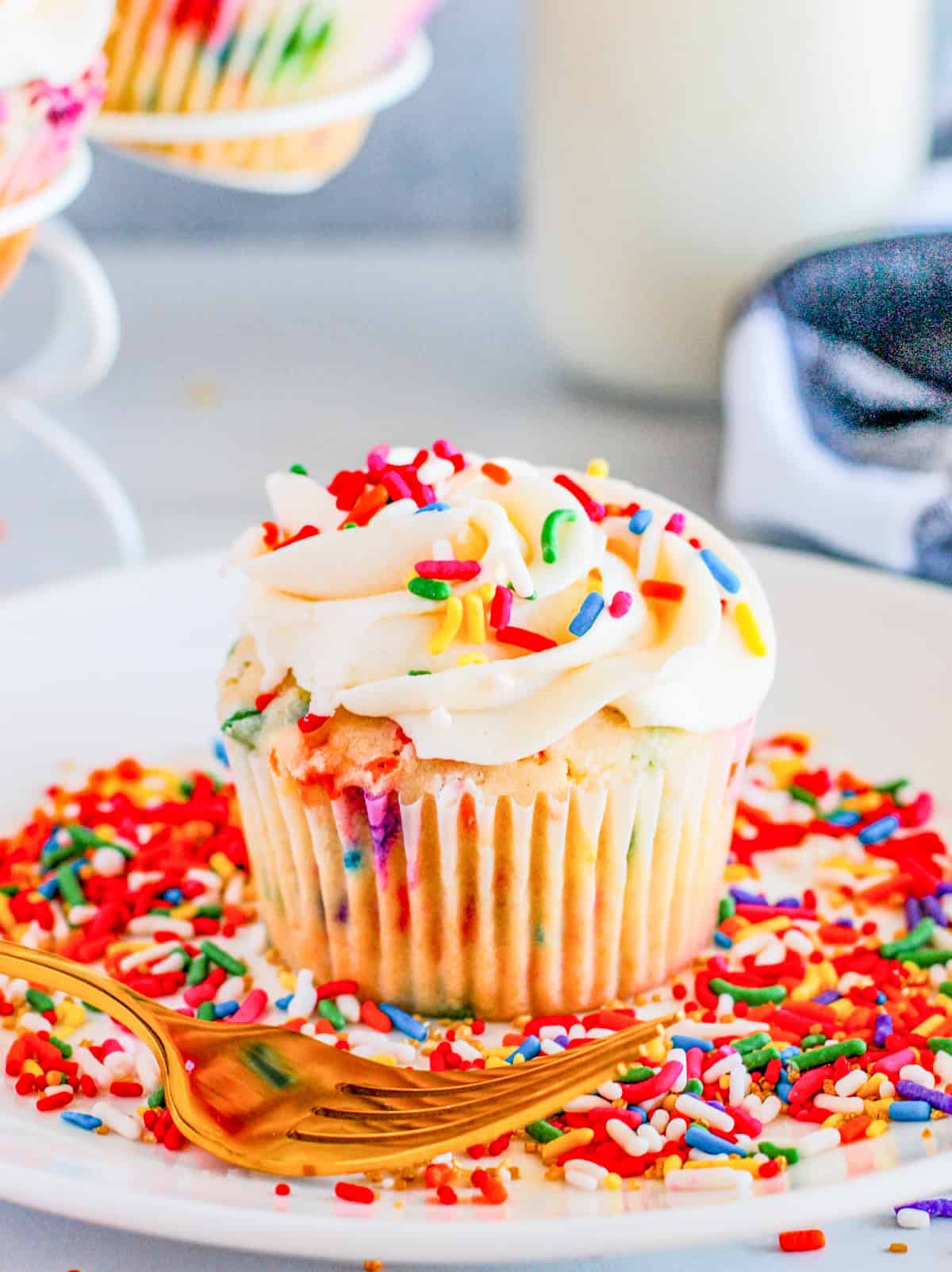 One of the Funfetti Cupcakes on a white plate with sprinkles and gold fork.