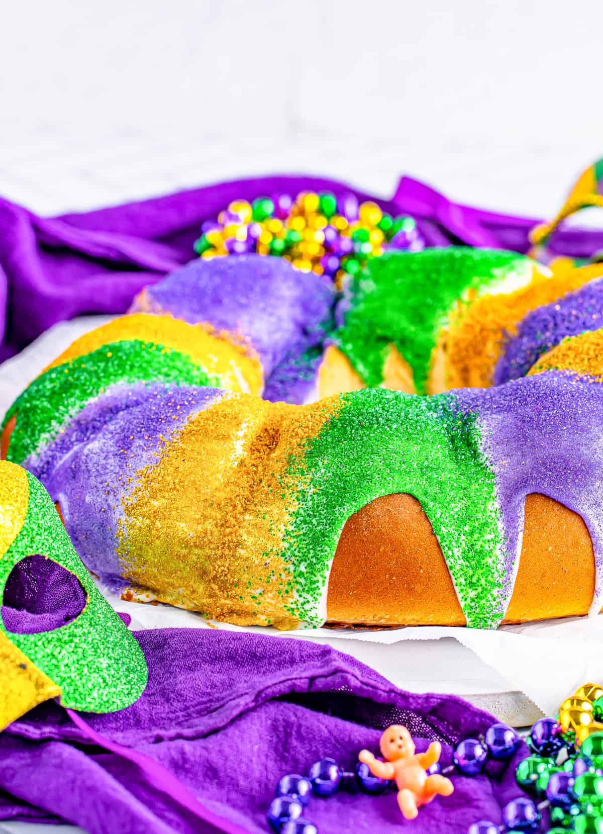 Finished and decorated King Cake Recipe on parchment paper with decorations surrounding cake.