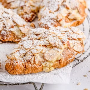 Close up square image of finished croissants on parchment paper on wire rack topped with powdered sugar.