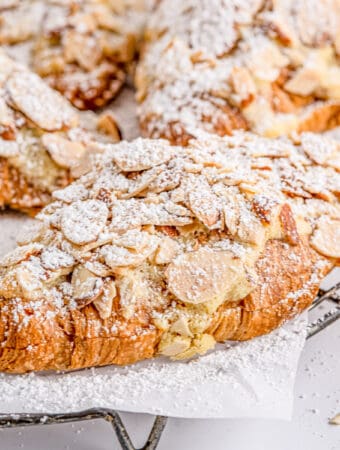 Close up square image of finished croissants on parchment paper on wire rack topped with powdered sugar.