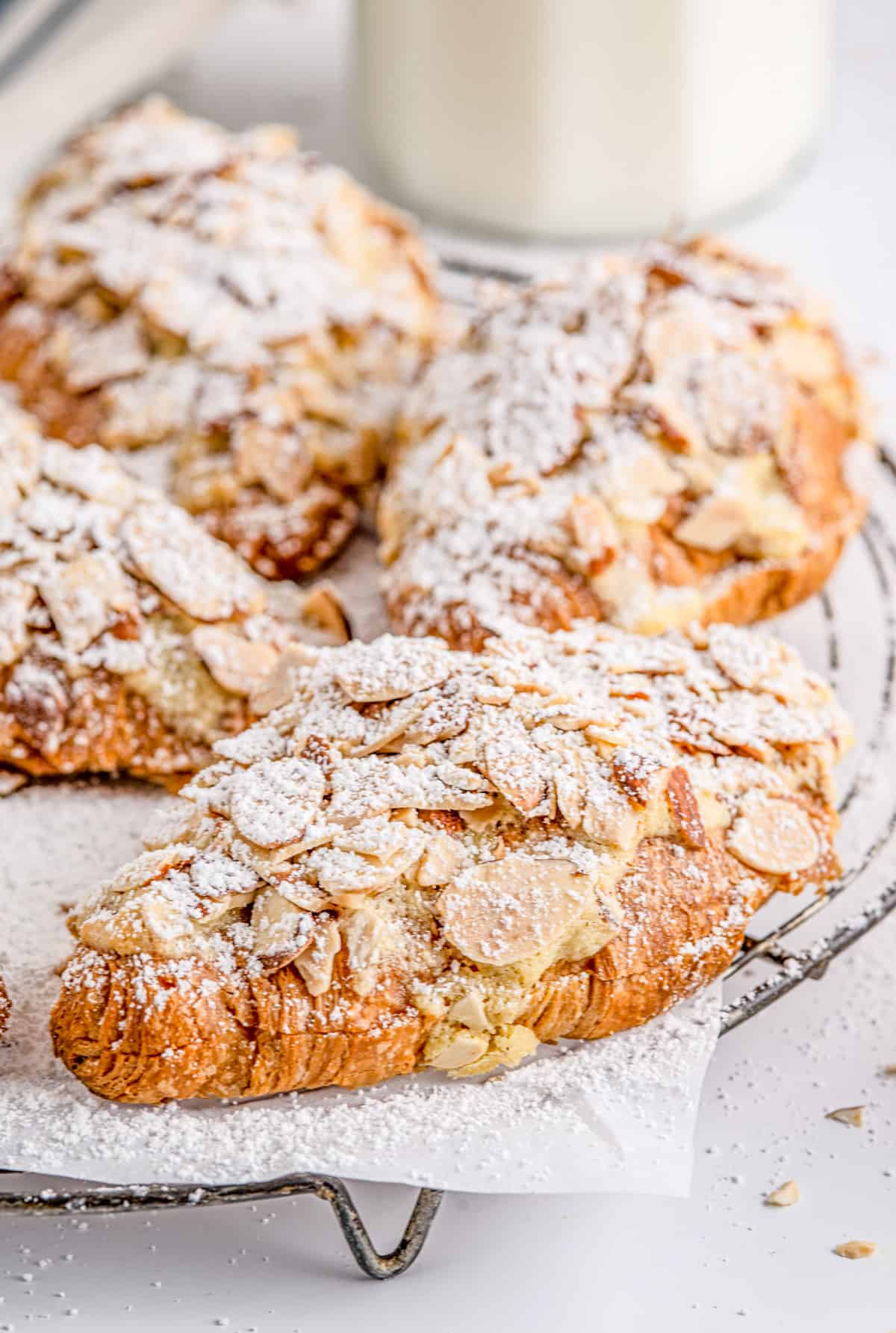 Almond Croissants on parchment paper on wire rack topped with powdered sugar.
