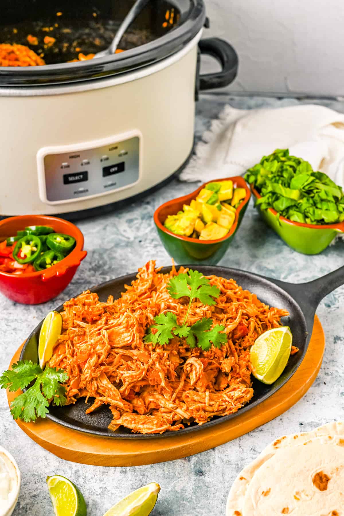 Plated Mexican Chicken on hot plate with slow cooker and serving options next to plate.
