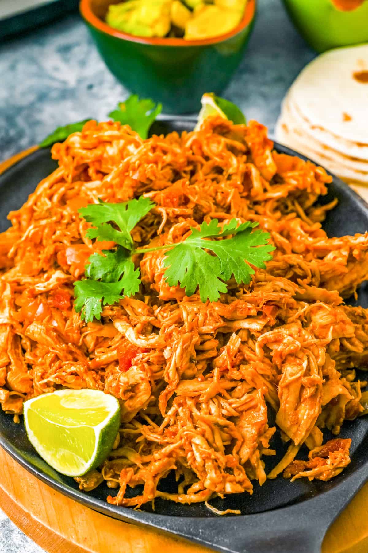 Slow Cooker Shredded Mexican Chicken on hot plate topped with cilantro and limes.
