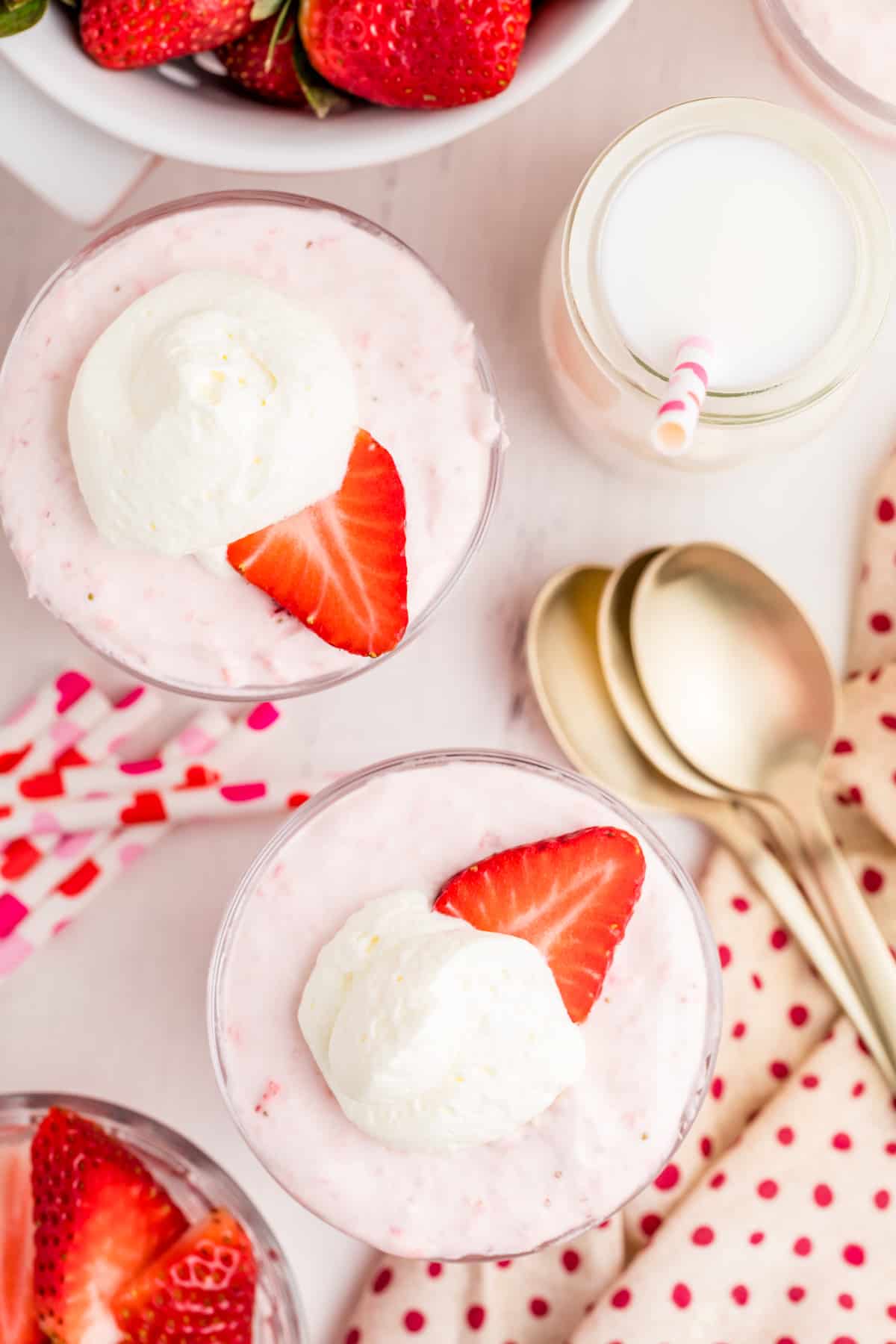 Overhead of Mousse in serving dishes topped with whipped cream and strawberry slices.