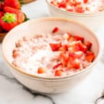 Close up photo of a bowl of oatmeal with diced strawberries and heavy cream drizzle on top.