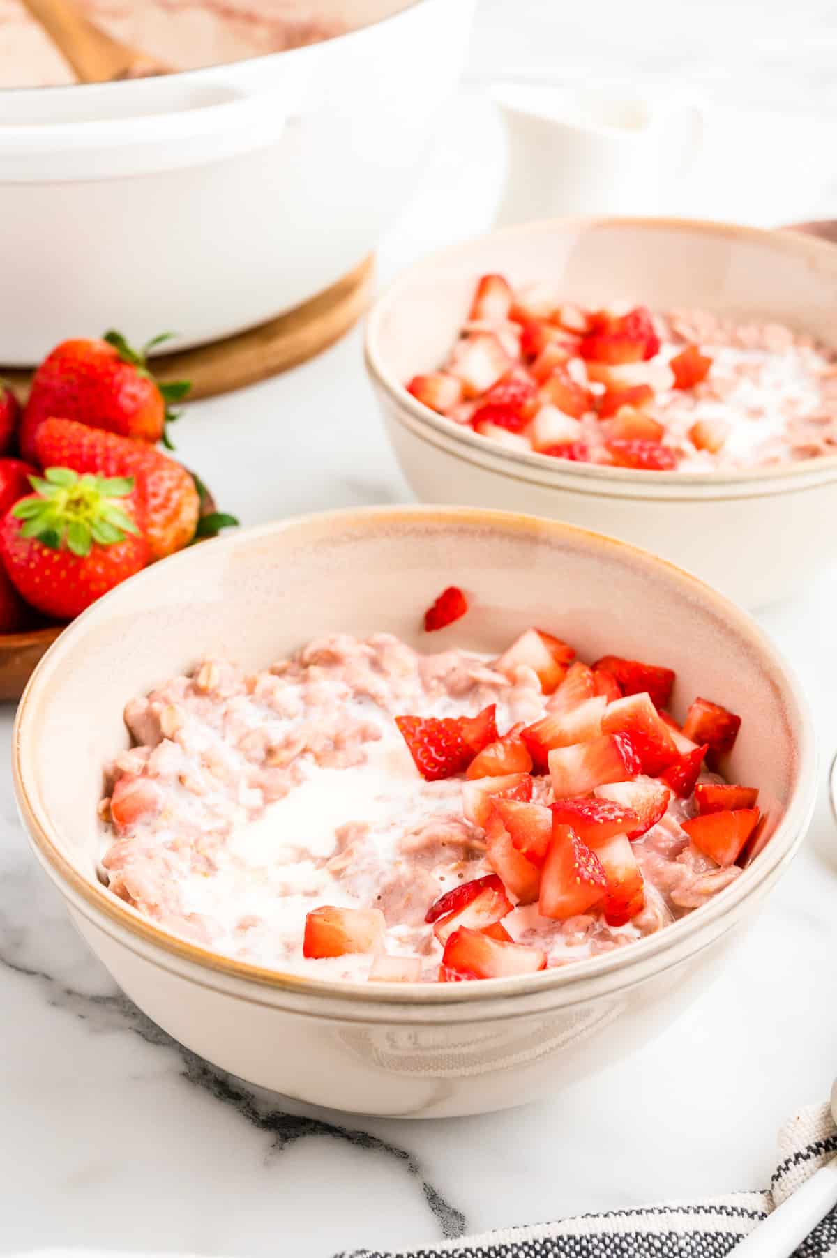 Two bowls of the Strawberry Oatmeal topped with diced strawberries and heavy cream.