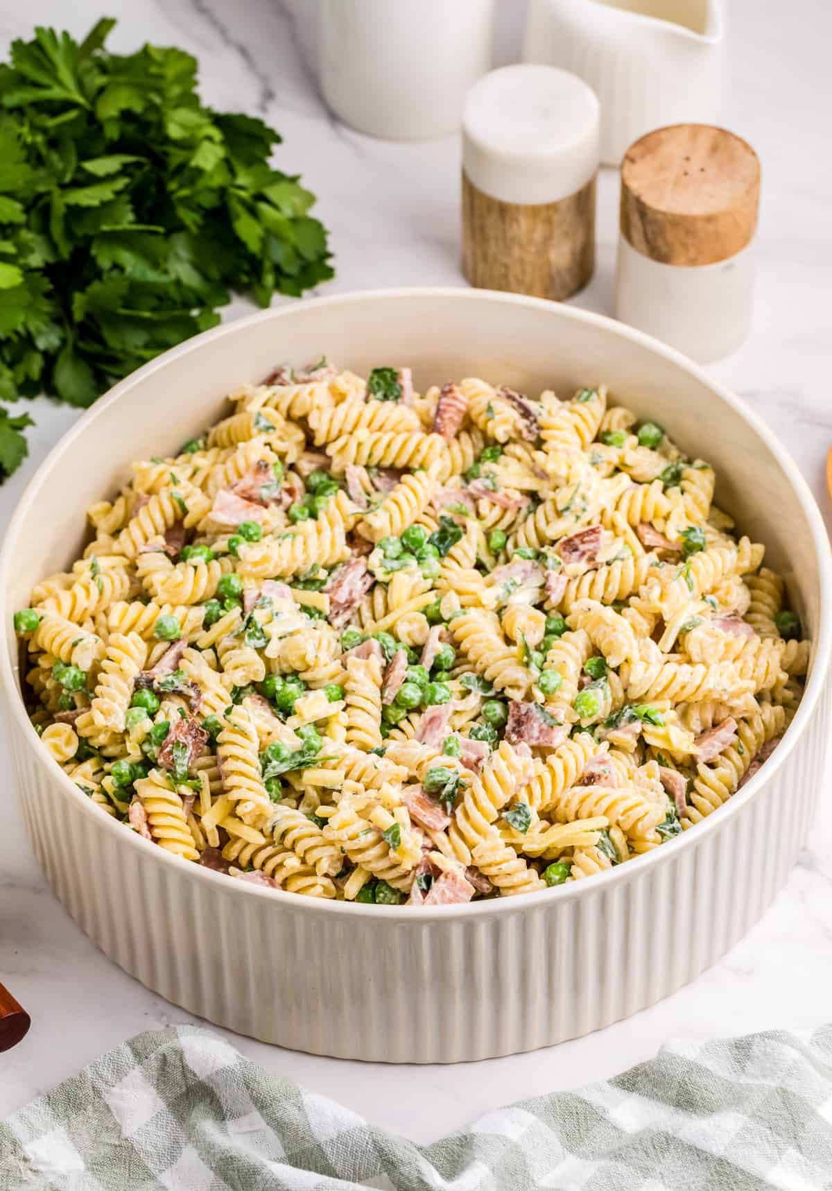 Bacon Ranch Pasta Salad in serving bowl with parsley, salt and pepper behind bowl.