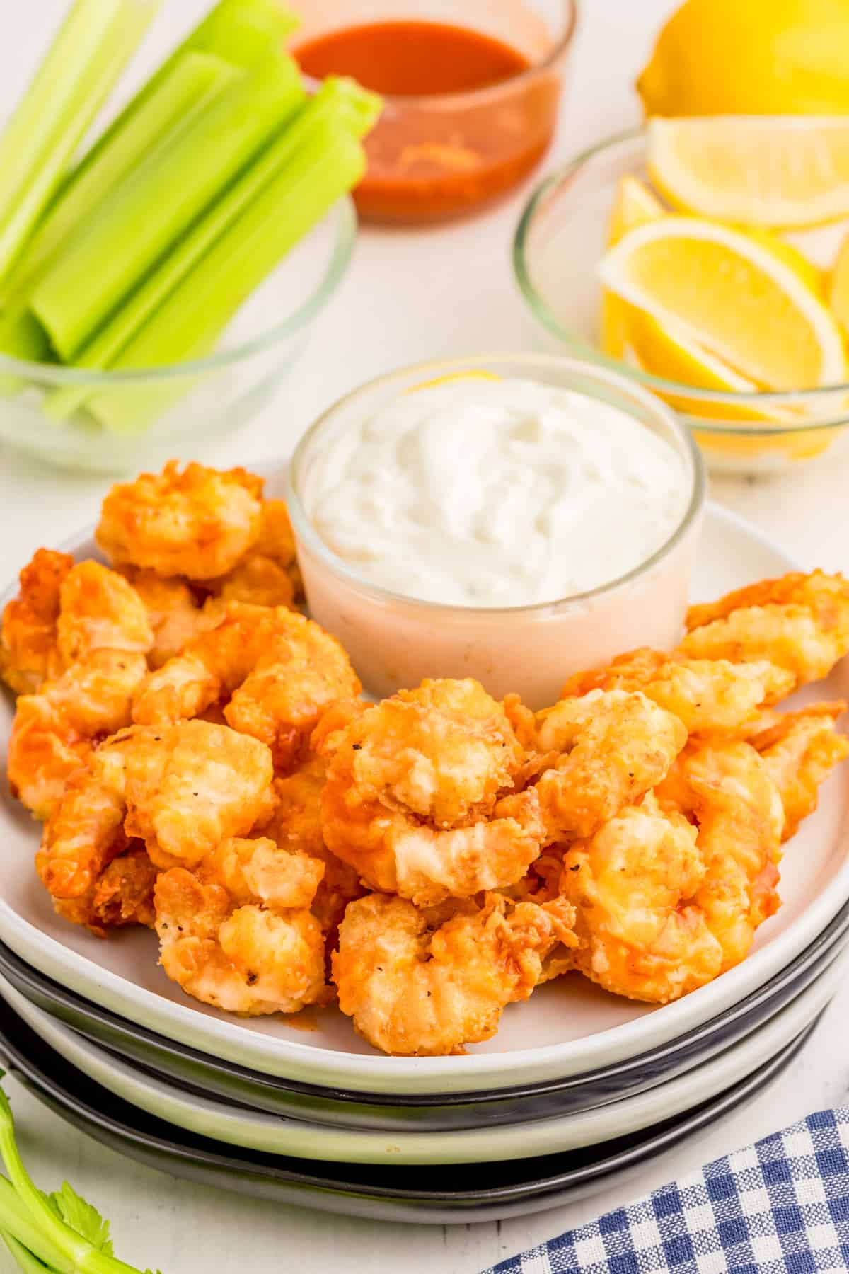 Buffalo Shrimp on stacked white plates with dipping sauce with celery buffalo sauce and lemons in background/