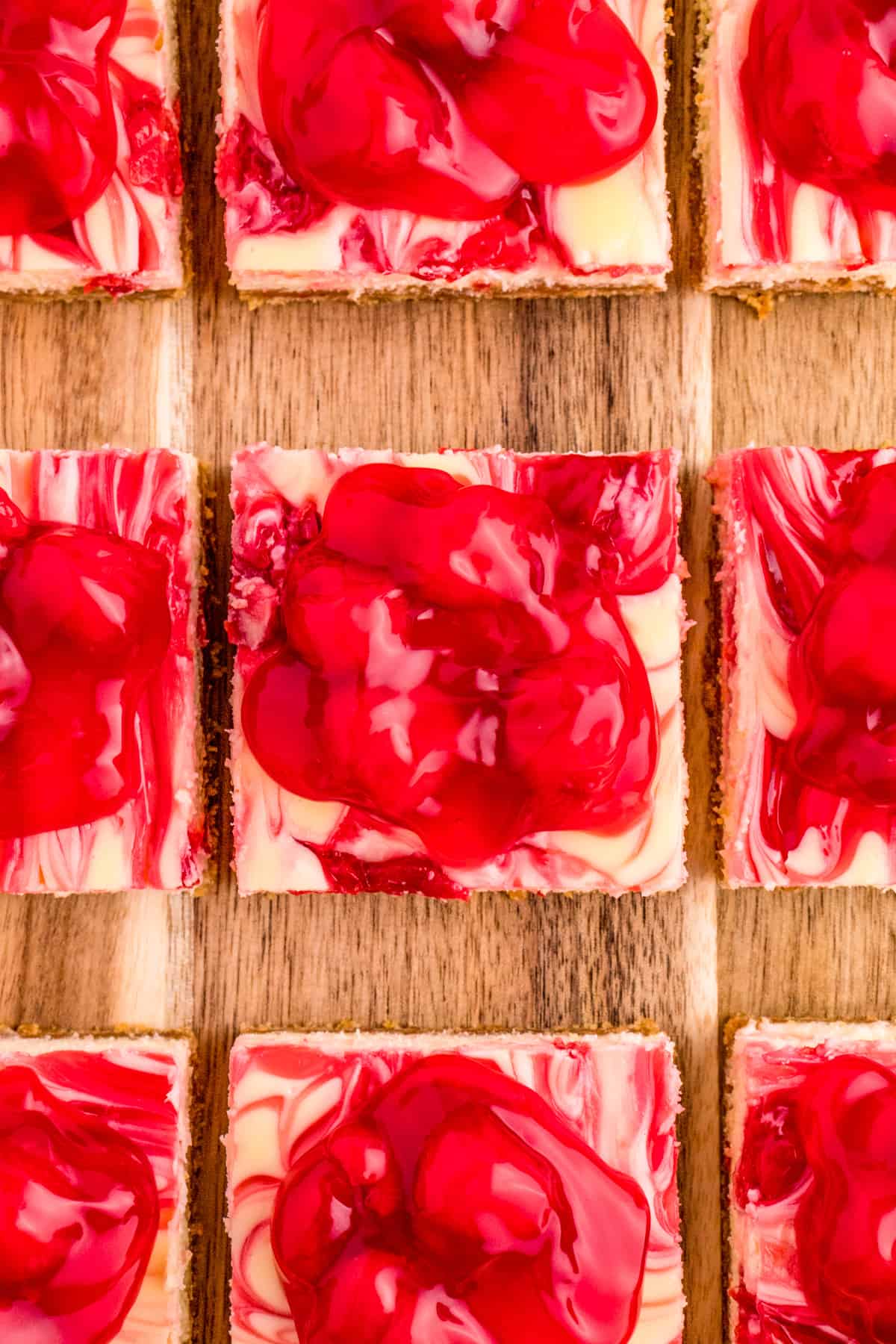 Overhead of Cheesecake Bars cut on wooden board topped with cherry pie filling.