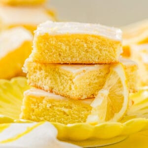 Close up square image of three stacked brownies on yellow plate with lemon slice.