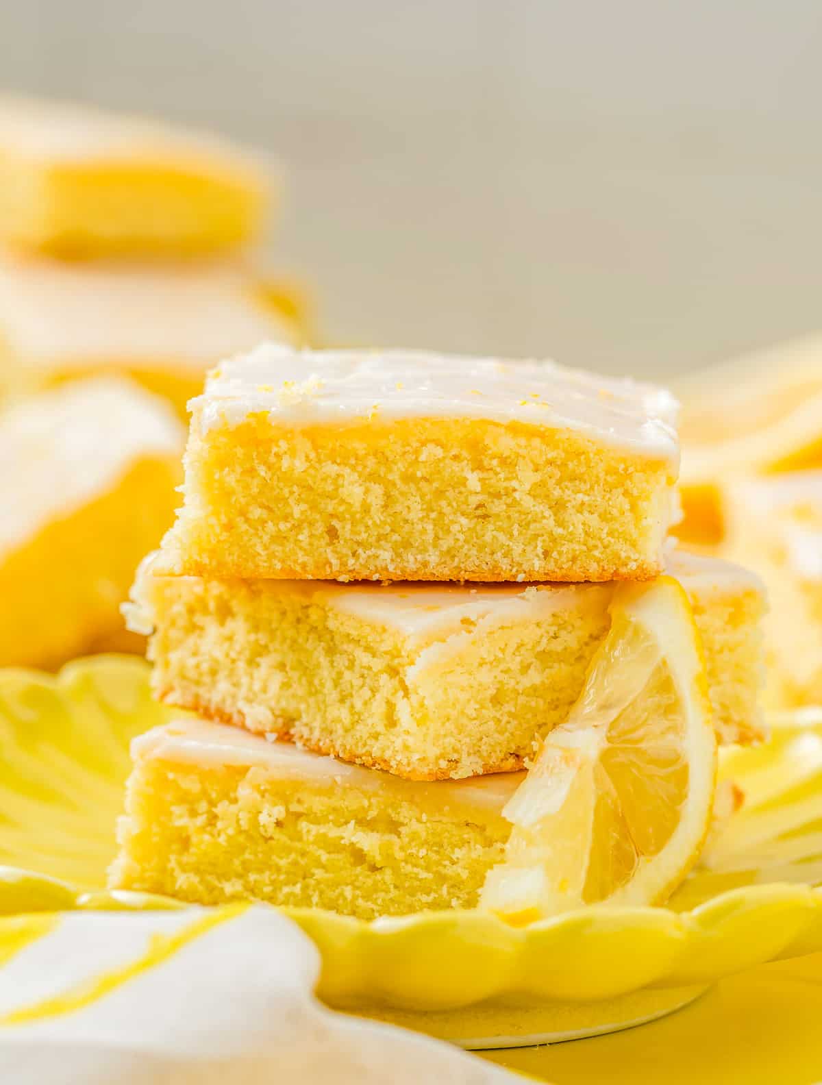 Three stacked Lemon Brownies on yellow plate with a lemon slice.