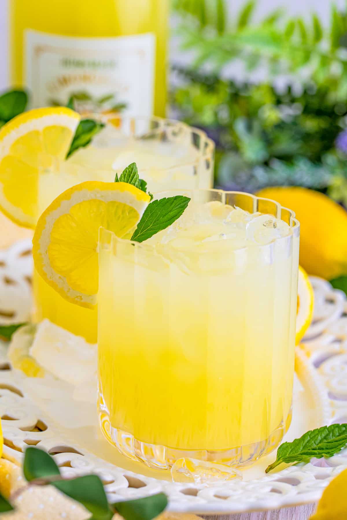 Limoncello Recipe on white platter with ice, lemon slice and mint.