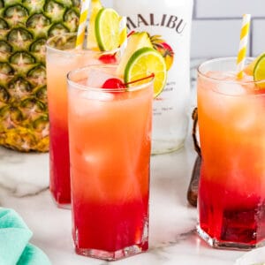 Square image of three finished cocktails with garnishes and malibu and pineapple in background.